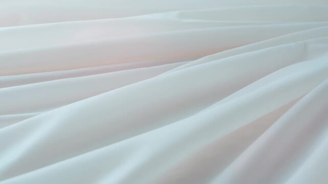 Shifting smooth pale fabric showing folds moving in studio close-up, soft light causing motion