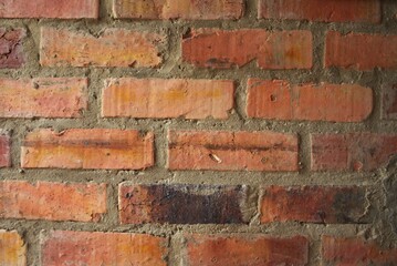 Fototapeta premium Full frame texture of a rustic red and orange brick wall with rough cement mortar