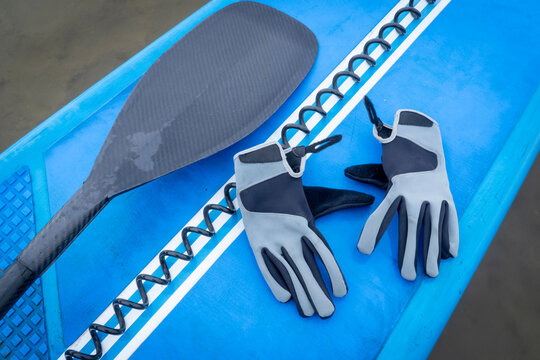 Paddling gloves, safety leash and paddle on a deck of stand up paddleboard - cold season paddling concept