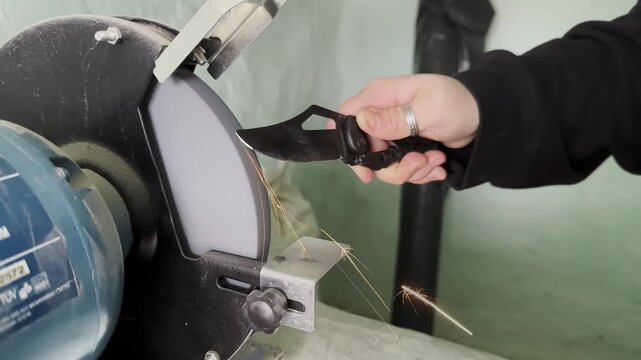 Person Sharpening Knife on Electric Grinder in Workshop