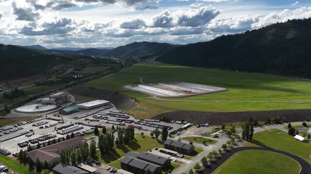 Aerial of industrial water treatment tanks and green fields near Kellogg Idaho with cloudy skies and mountain views