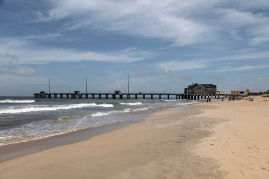 Public concrete pier extending into ocean surf from sandy beach