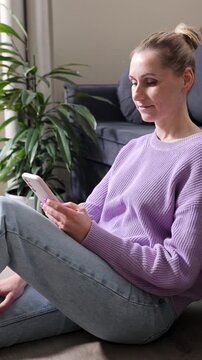 woman scrolling internet website on mobile phone while sitting on the floor in living room at home. online shopping