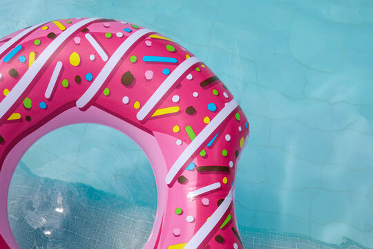 Close-up of the curved edge of a pink donut float with sprinkle decorations, floating on sparkling turquoise pool water