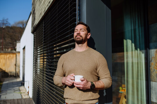 Relaxed man drinking coffee on terrace at home on sunny day.
