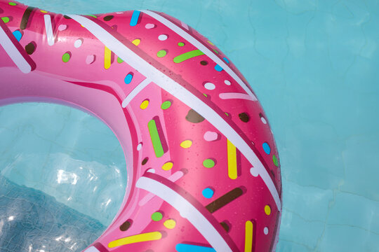 Close-up of a pink donut-shaped inflatable float with sprinkle patterns, floating on bright turquoise pool water