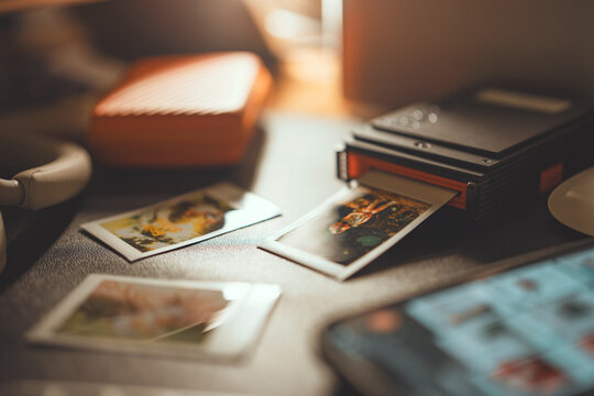 Close up of portable smartphone printer printing instant photo on table, wireless photo printer with polaroid style prints in warm morning light for photography gadget, memory, and hobby concept