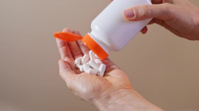 Woman pouring white tablets from bottle into hand in close-up on beige background. Vitamins support daily nutrition, dietary balance and wellness routines designed for healthy lifestyle communication