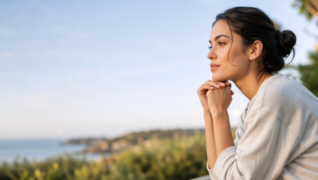 Profile portrait of a young woman looking at the ocean. Thoughtful female resting chin on hands with a blurred coastal background. Copy space