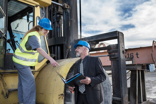 Matures boss with portfolio talking with worker woman who is drinving bulldozer in construction site