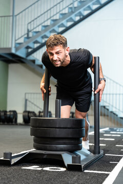 Determined man pushing heavy sled during intense gym workout
