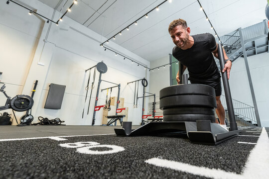 Strong man pushing weighted sled in modern gym