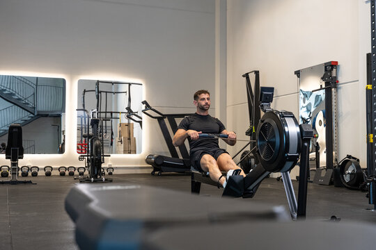 Determined man training on rowing machine in modern gym