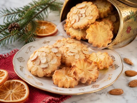 Norwegische Weihnachtspl&auml;tzchen mit Mandeln auf Vintage-Teller und aus Keksdose, festliche Foodaufnahme in heller Winterstimmung