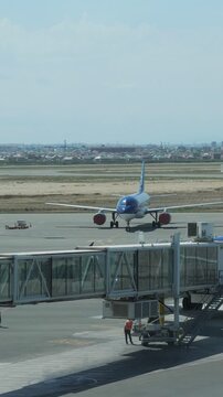 Commercial airliner moving away from the passenger boarding bridge on the tarmac, preparing for departure and taxiing on the runway with ground crew staff working under a clear blue sky