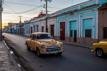 Fototapeta premium Yellow vintage car driving through a street in Cienfuegos