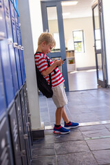 Schoolboy leaning against blue lockers in school hall, wearing red-and-white tee using smartphone © wavebreak3