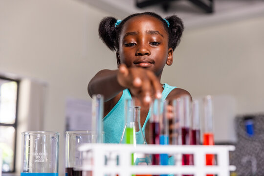 African American child girl reaching toward white test tube rack with colored liquids at lab table