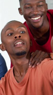 Vertical video: Moving blue phone, man in orange tee framing group in red tank in room for selfie