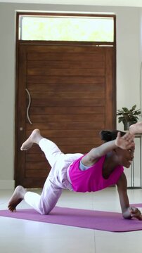 Vertical video: Kneeling youth in pink tank balancing on purple mat in entry, mirroring partner