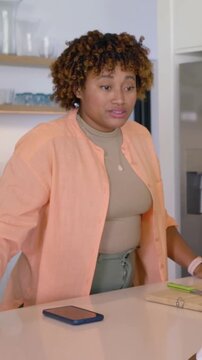 Vertical video: Talking to off-camera person, peach-top woman pouring juice from carafe in kitchen
