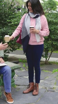 Vertical video: Entering from left, woman carrying two coffees, offering cup while meeting friend