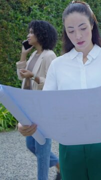 Vertical video: Walking woman in blazer taking call on gravel path, joining peer reviewing plans