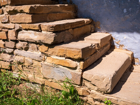 Weathered stone steps leading to a traditional rural house. Rustic architecture detail with natural sandstone blocks, sunlight, and authentic countryside atmosphere.