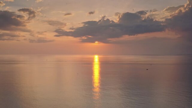 Sunset light paints sky and tranquil ocean waves, reflecting golden sun path on water's surface, creating peaceful and serene tropical landscape with a vast expanse of sea and sky. Natural background