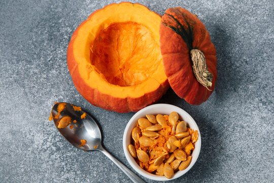 Pumpkin carving process showing hollowed pumpkin and seeds on a table in a kitchen setting during fall season