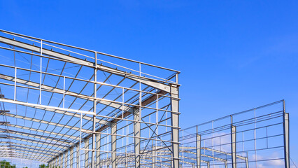 Naklejka premium Metal framework of industrial warehouse buildings structure in construction site against blue sky background, low angle view