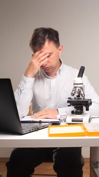 Vertical video scientist carefully preparing a sample for microscopic examination while working at a modern lab desk with a laptop and clipboard, focused on scientific study and detailed analysis