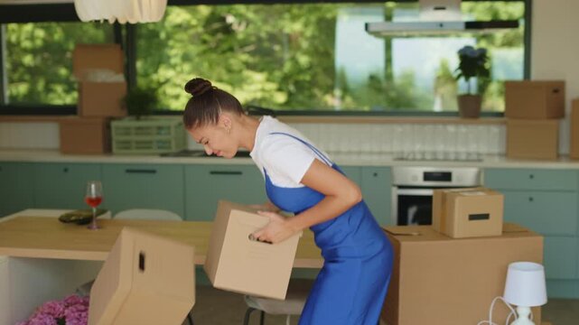 Young woman suffering while carrying stack of moving boxes in new home