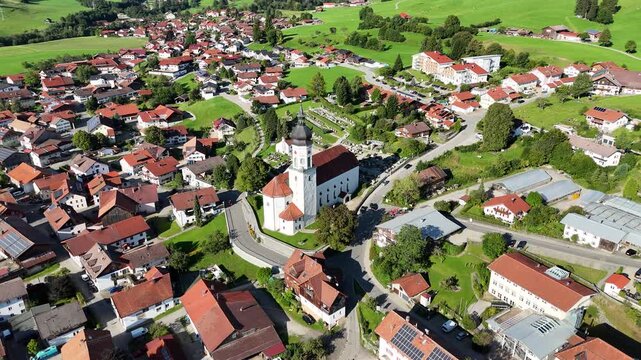 Orbit flight around parish church St. Ulrich in village Wertach with houses and meadows in Allg&auml;u Alps, Bavaria, Germany