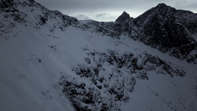 Aerial view of steep snow-covered mountain ridge under overcast sky