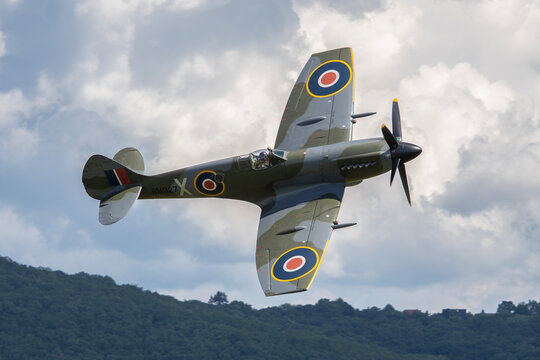 MLADA BOLESLAV, CZECH REPUBLIC - JUNE 13, 2026: A historic Supermarine Spitfire Mk XIV (registration RM927) fighter aircraft performing a steep banking turn against a backdrop of clouds at an airshow.