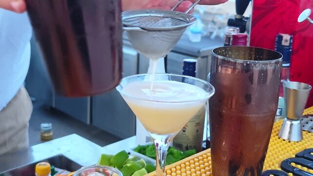 Professional man bartender pouring cocktail drink in cocktail glass from a shaker. Beach bar.