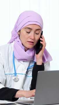 Medical Professional On Call. Healthcare Specialist Reviewing Patient Information Remotely. Female Medical Practitioner Focused On Telehealth Session With Notes And Equipment Visible On Desk