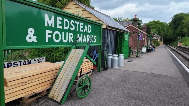 Hampshire England UK. 03.06.2026. Video. A picturesque vintage train station platform featuring a traditional wooden trolley, stacked lumber, and classic railway tracks under a cloudy sky
