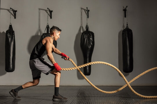 Young Hispanic boxer performing battle rope waves during training session