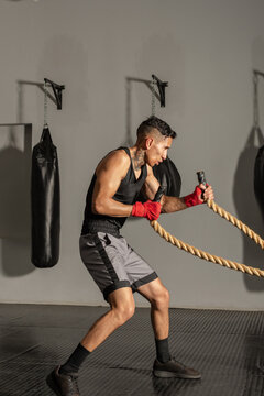 Young Hispanic boxer training with battle ropes in gym