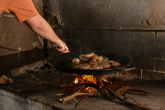 Man stirring chicken in Valencian paella over wood fire