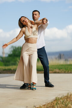 Romantic couple dancing outdoors on a sunny day, woman leaning back in her partner's embrace during a slow dance