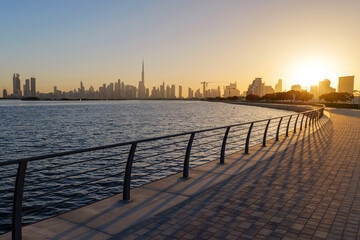 Obraz premium Sunset view from Al Jaddaf Walk waterfront promenade overlooking Dubai skyline and Burj Khalifa, with golden evening light reflecting across Dubai Creek