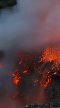 Vertical video: Erupting lava fountain, gas release forcing molten rocks up at vent rim, with steam