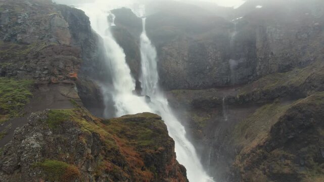 Majestic aerial view of the Rjukandafoss waterfall flowing through a rocky canyon on a foggy day. The powerful cascade is a hidden gem