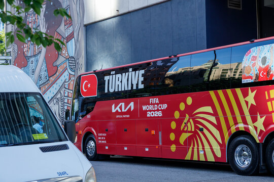 The red Turkiye team bus, its side wrapped with a golden crest and FIFA World Cup 2026 graphics, parked beside an indigenous mural in a downtown loading area.