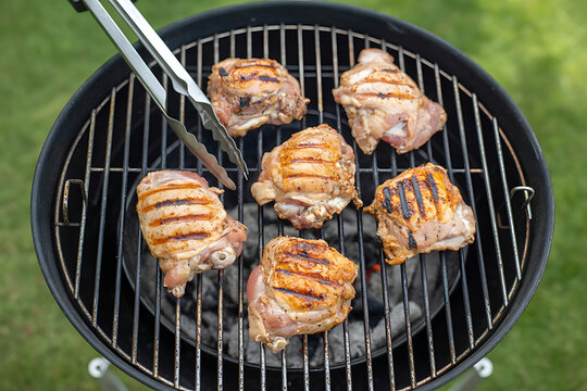 Grilled chicken thighs cooking on barbecue grill with smoke and char marks outdoor summer meal