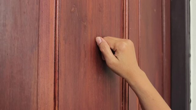 Short clip of female hand making a knocking gesture on a brown timber door, silent footage.
