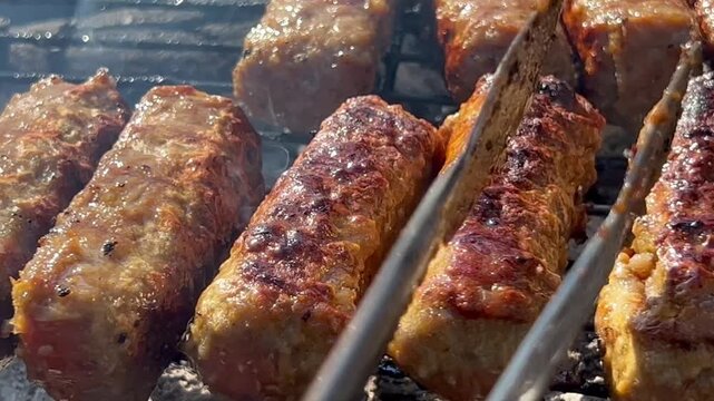 Close up macro shot of traditional Turkish Tekirdag meatballs sizzling and smoking on hot outdoor charcoal grill during backyard barbecue picnic.